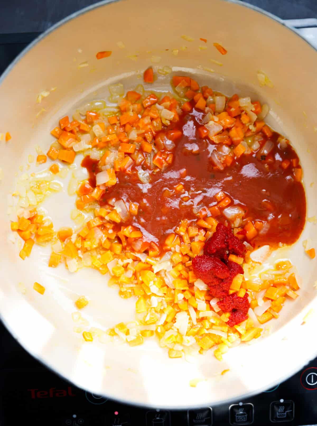 A pot with cooked onions, garlic and carrots and tomato paste and sauce added to it.