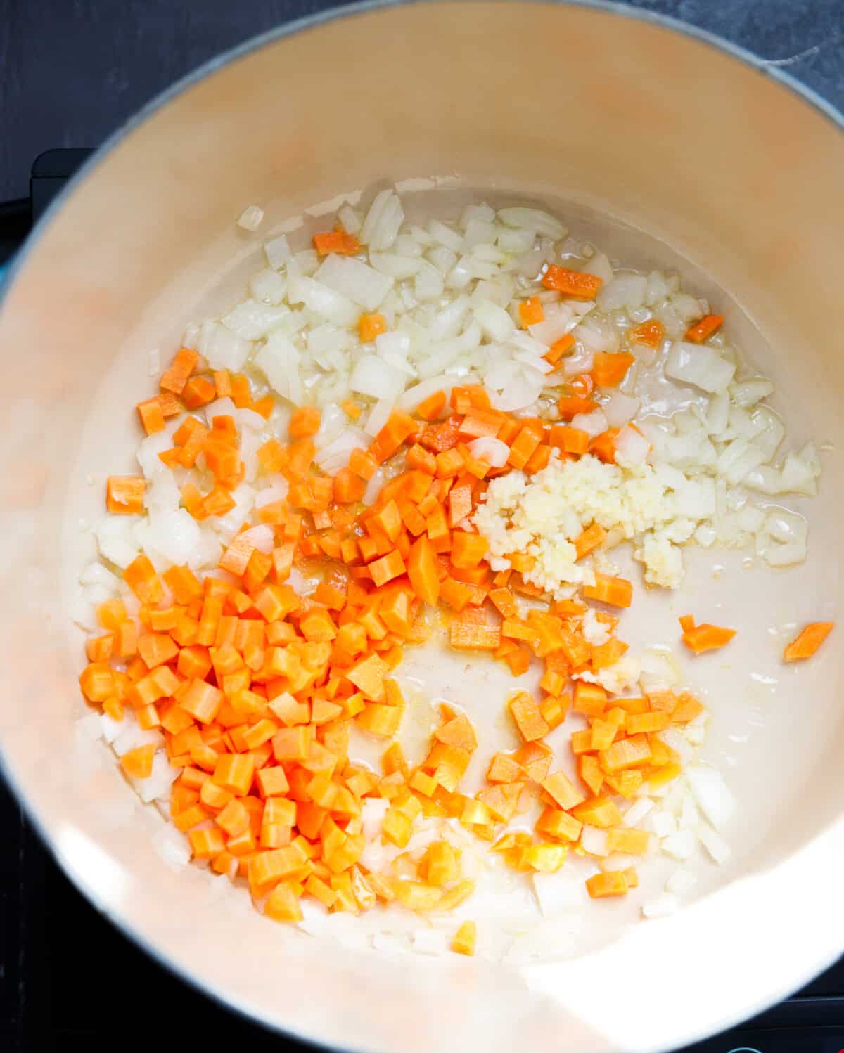 A Dutch oven with oil, onion, garlic and carrot inside