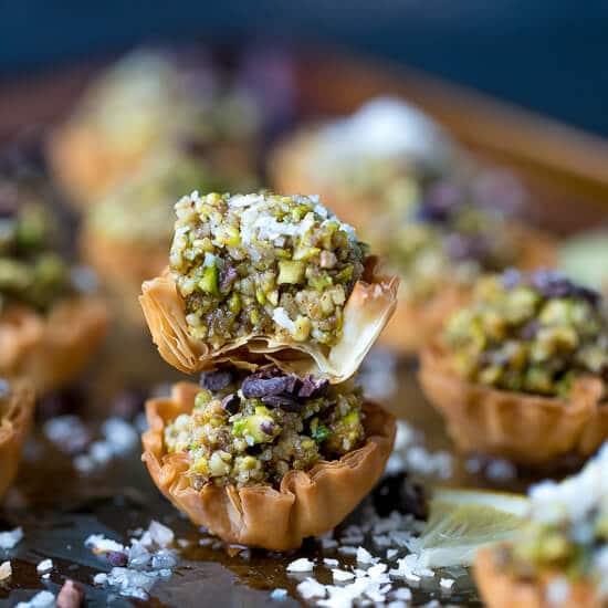 A tray with mini phyllo baklava cups, colorful and flakey, topped with coconut flakes.