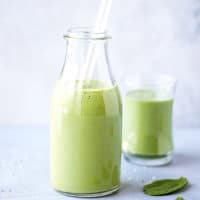 Spirulina Smoothie Recipe in a tall clear glass, with spinach and hemp seeds on the side.