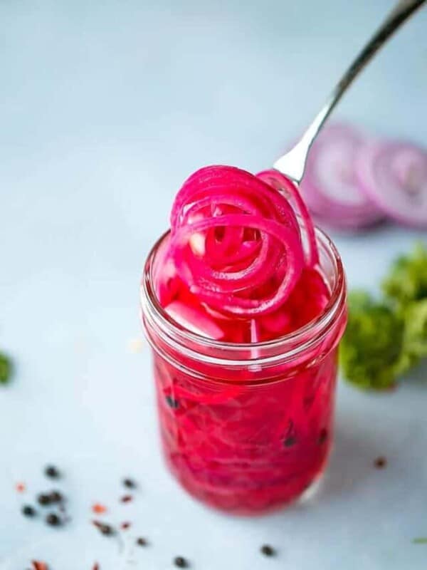A small glass jar with bright colorful pickled red onions. Purple onions with vinegar, salt and sugar,