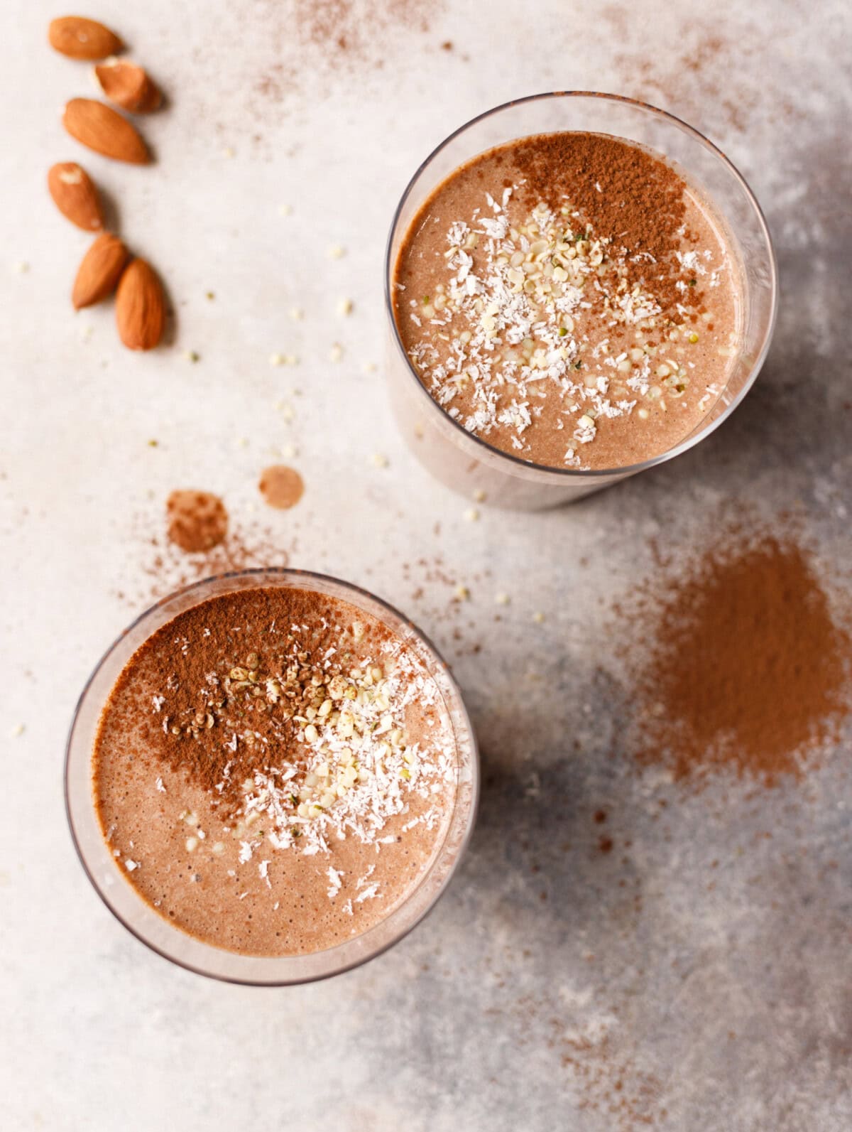 Almond coffee protein smoothie in two glasses topped with cocoa powder, coconut and seeds