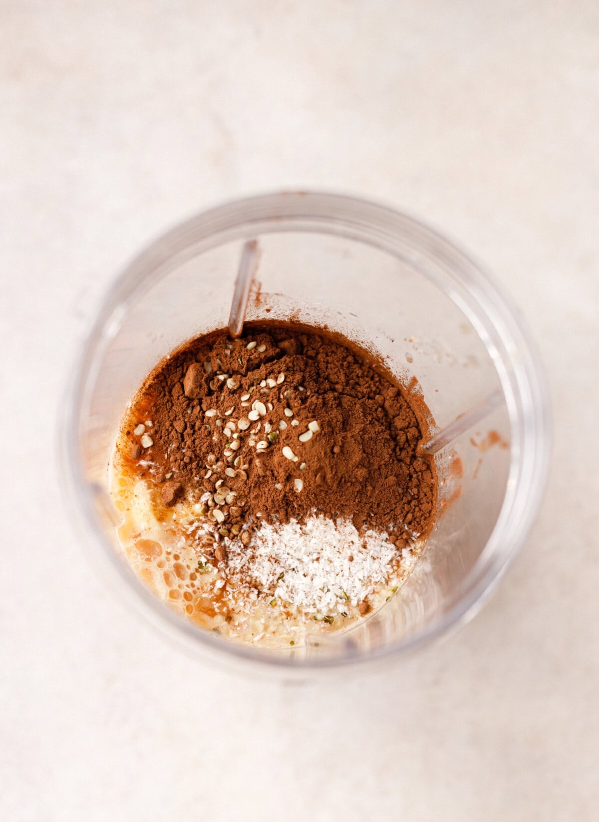 Almond coffee smoothie ingredients in blender with cocoa powder, coconut, seeds and milk before blending