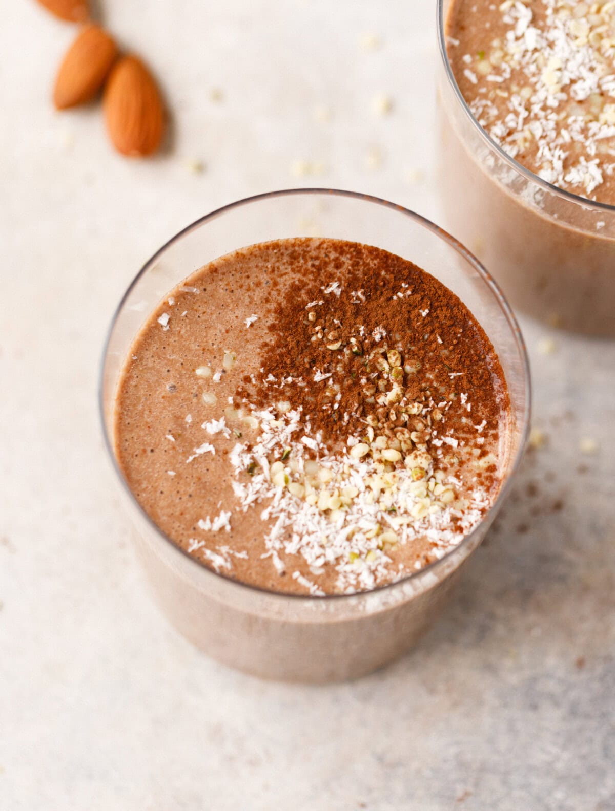 Almond coffee protein smoothie topped with cocoa powder, coconut and seeds in a glass