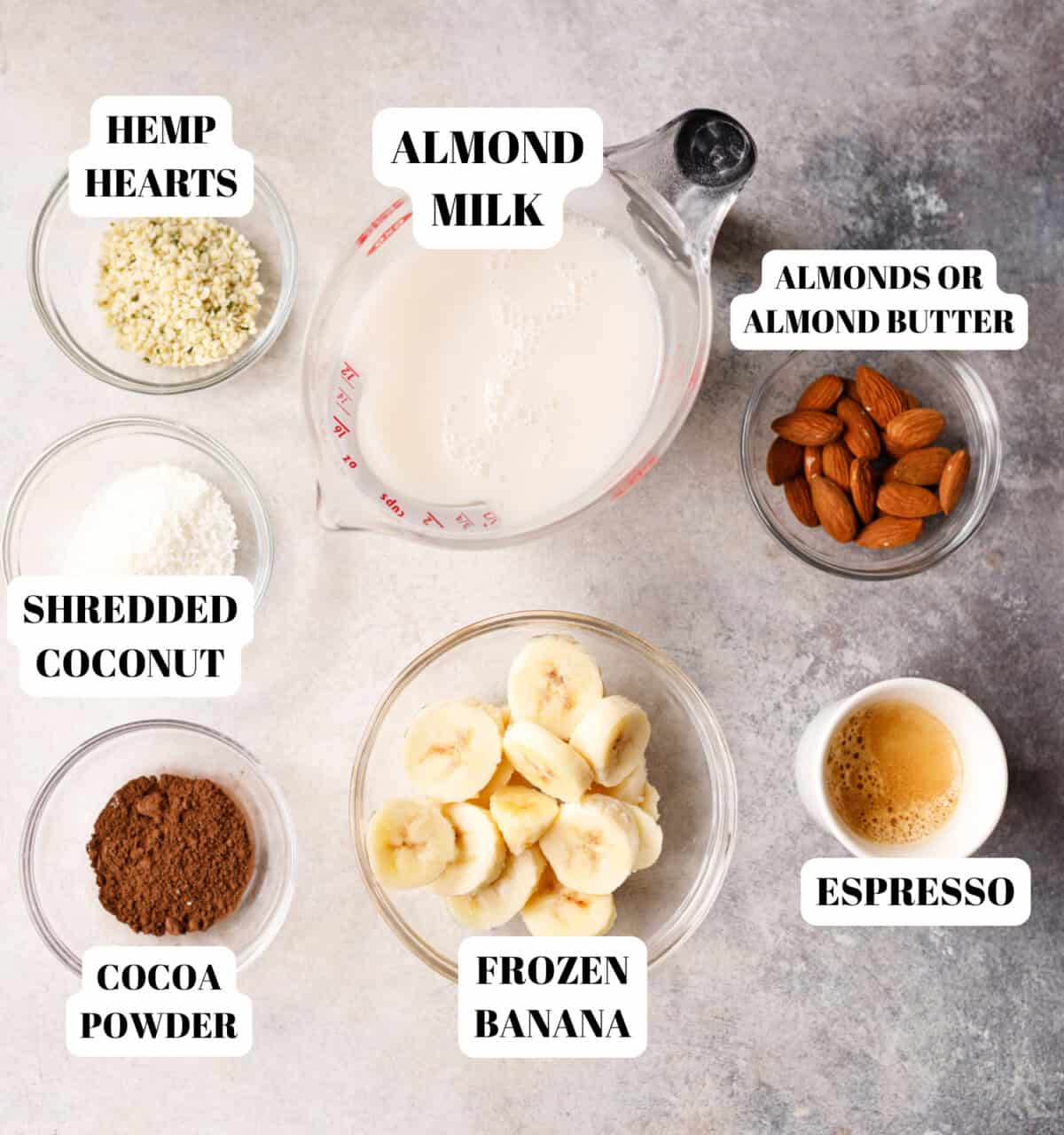 Ingredients for almond coffee protein smoothie including almond milk, banana, cocoa powder, espresso, almonds, coconut and hemp hearts