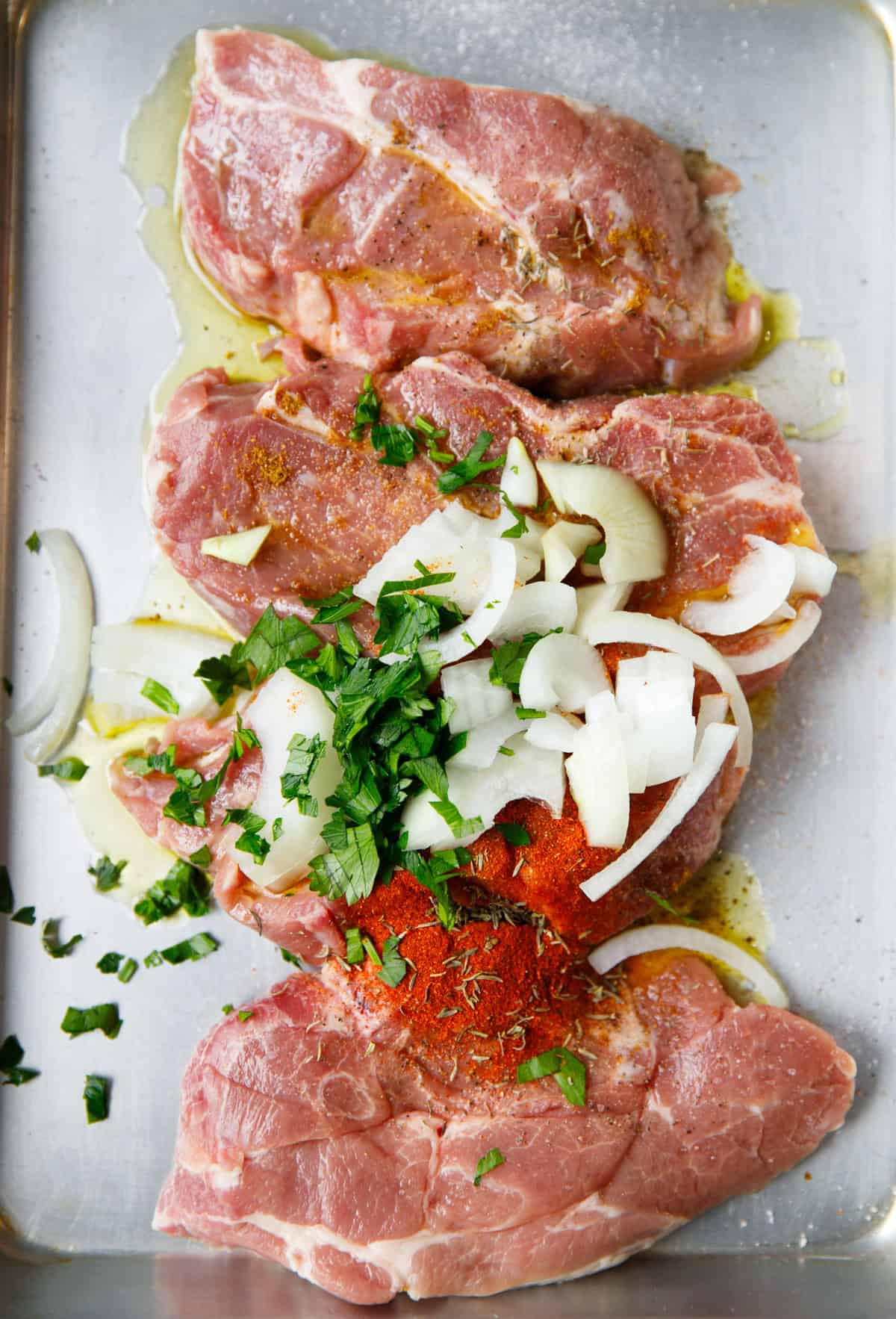 Pork shoulder steaks with olive oil, spices, onions and parsley before marinating