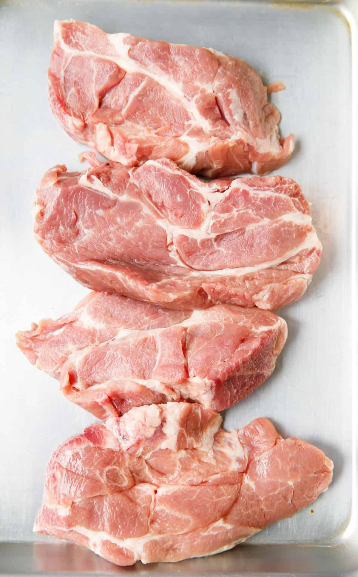 Raw pork shoulder steaks on metal tray before seasoning