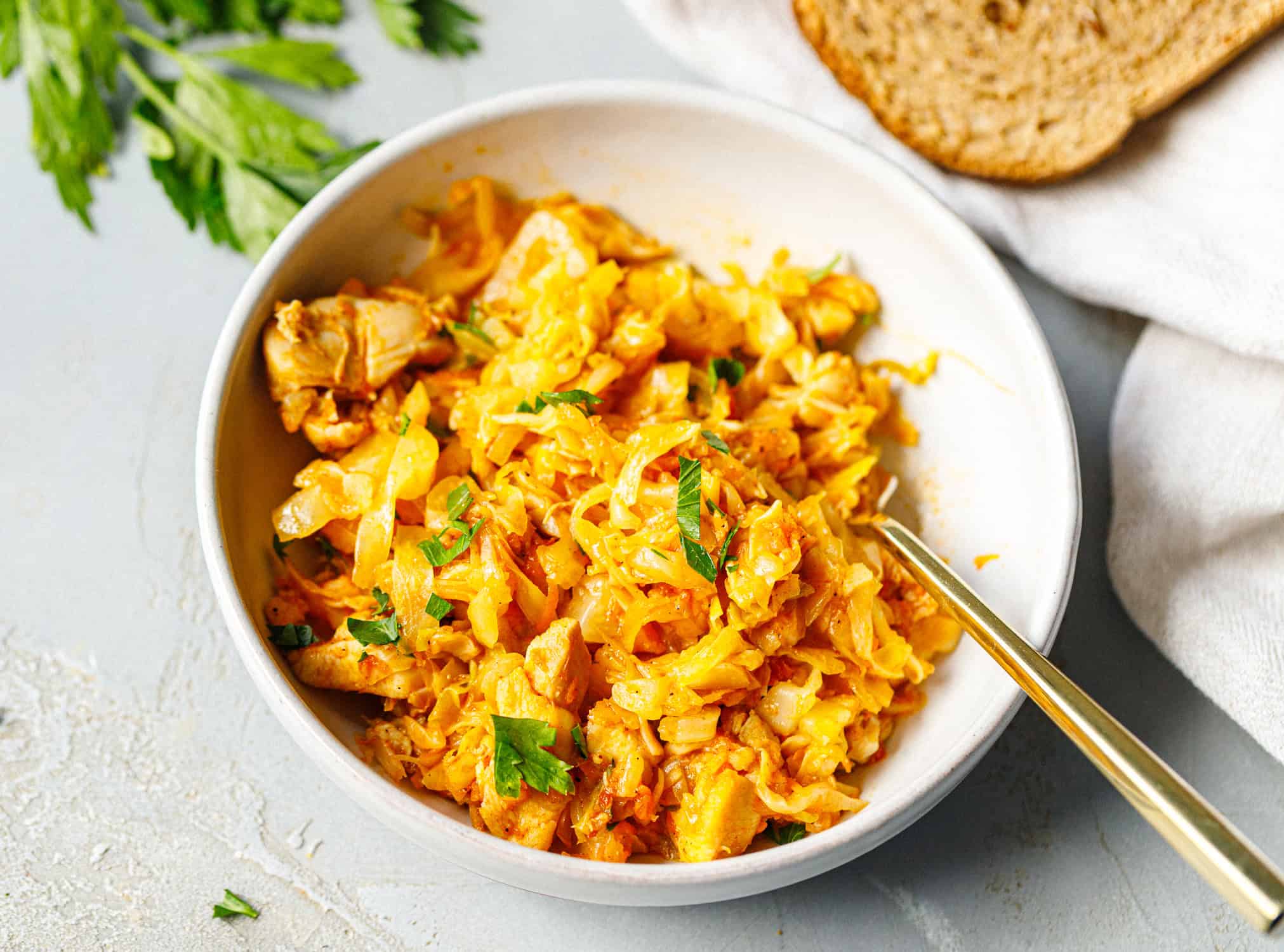 Bowl of chicken and cabbage with fresh parsley, a gold fork and a slice of bread