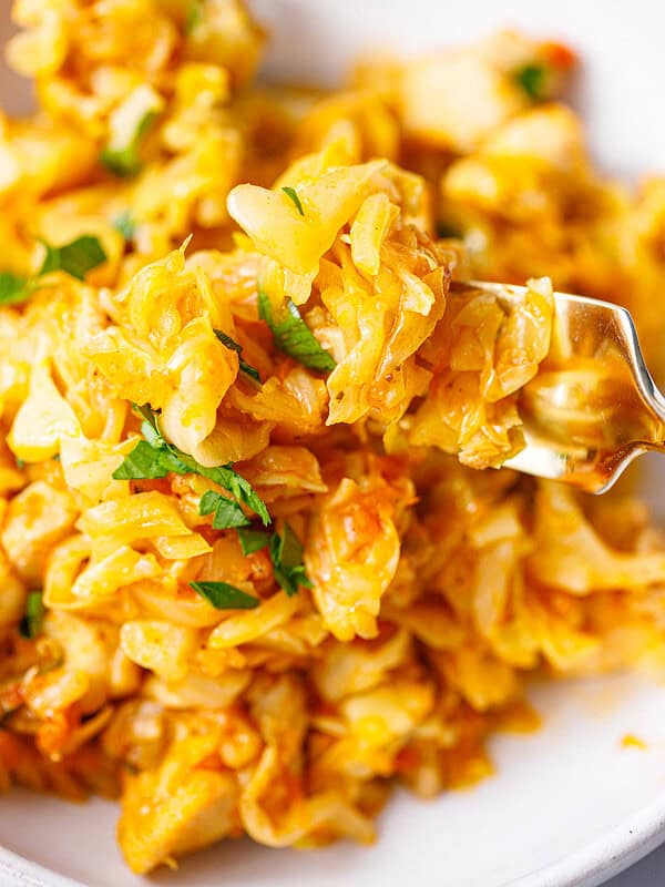 Fork lifting a bite of chicken and cabbage with chopped parsley