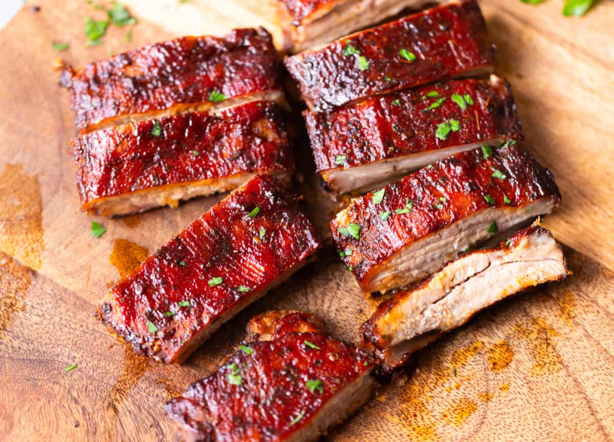 Juicy oven-baked St. Louis style ribs sliced on a wooden board and brushed with glossy barbecue sauce.
