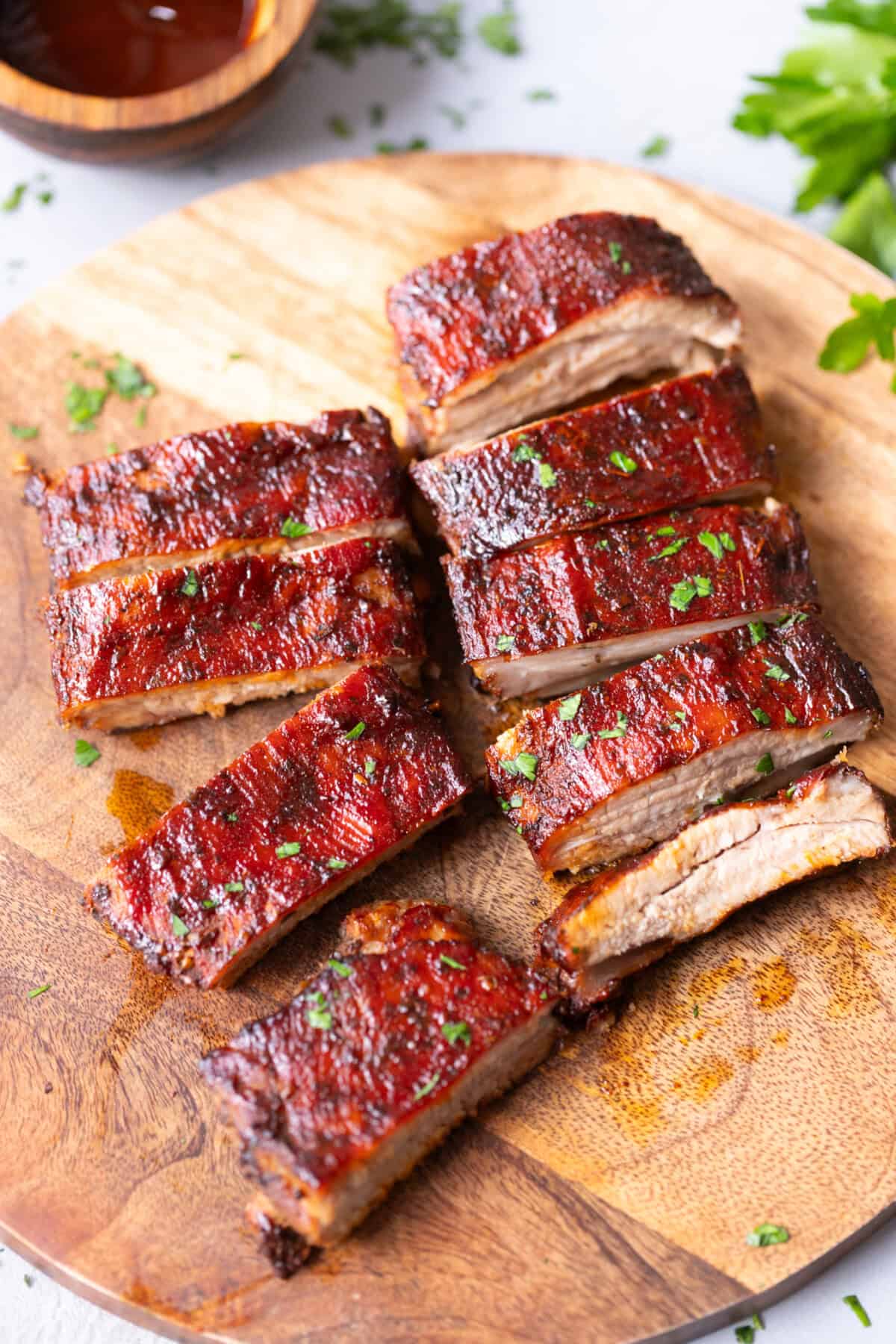 Juicy oven-baked St. Louis style ribs sliced on a wooden board, coated in glossy barbecue sauce and sprinkled with fresh parsley.