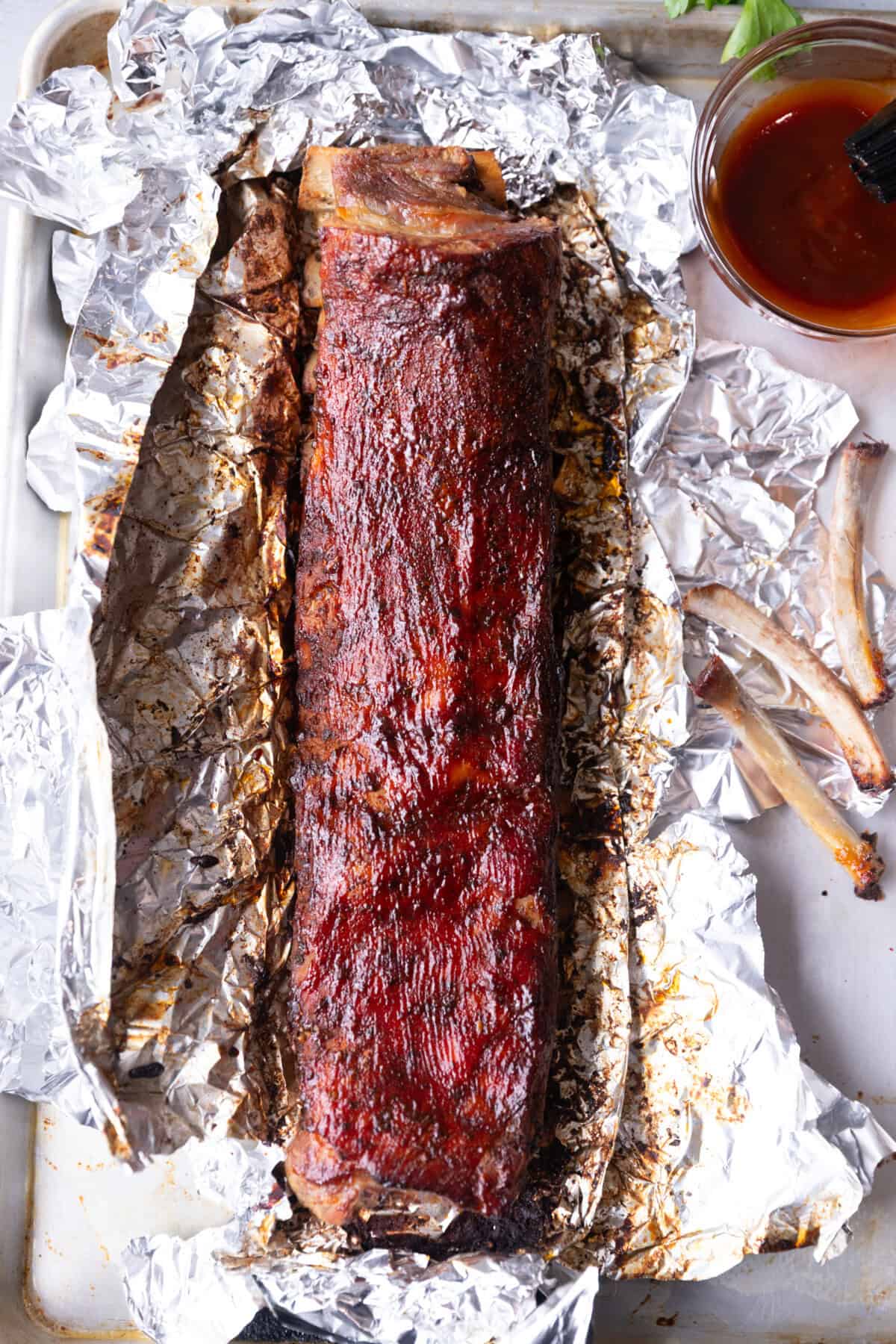 Baked and brushed with BBQ sauce St Louis ribs on aluminum foil, fall off the bone