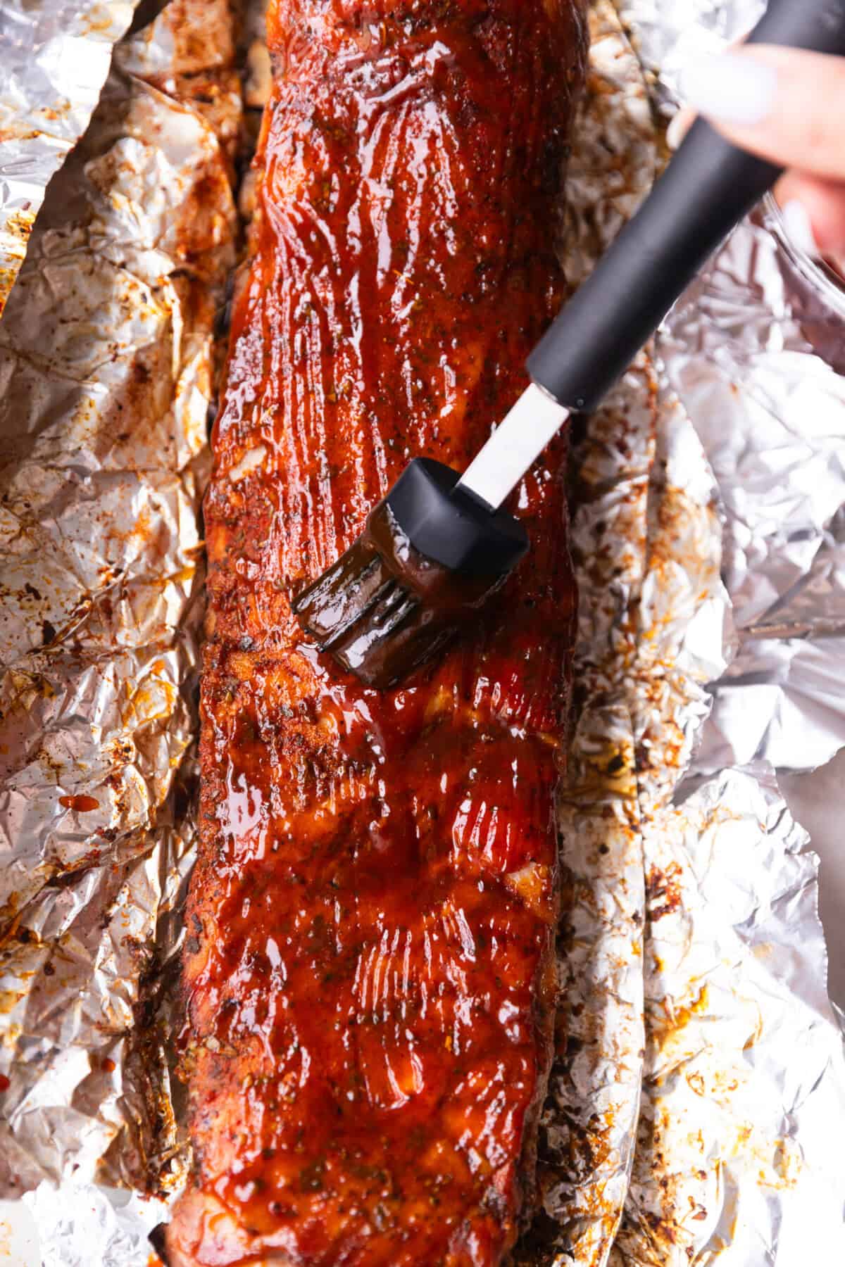 Brushing barbecue sauce over baked St. Louis style ribs with a silicone brush.