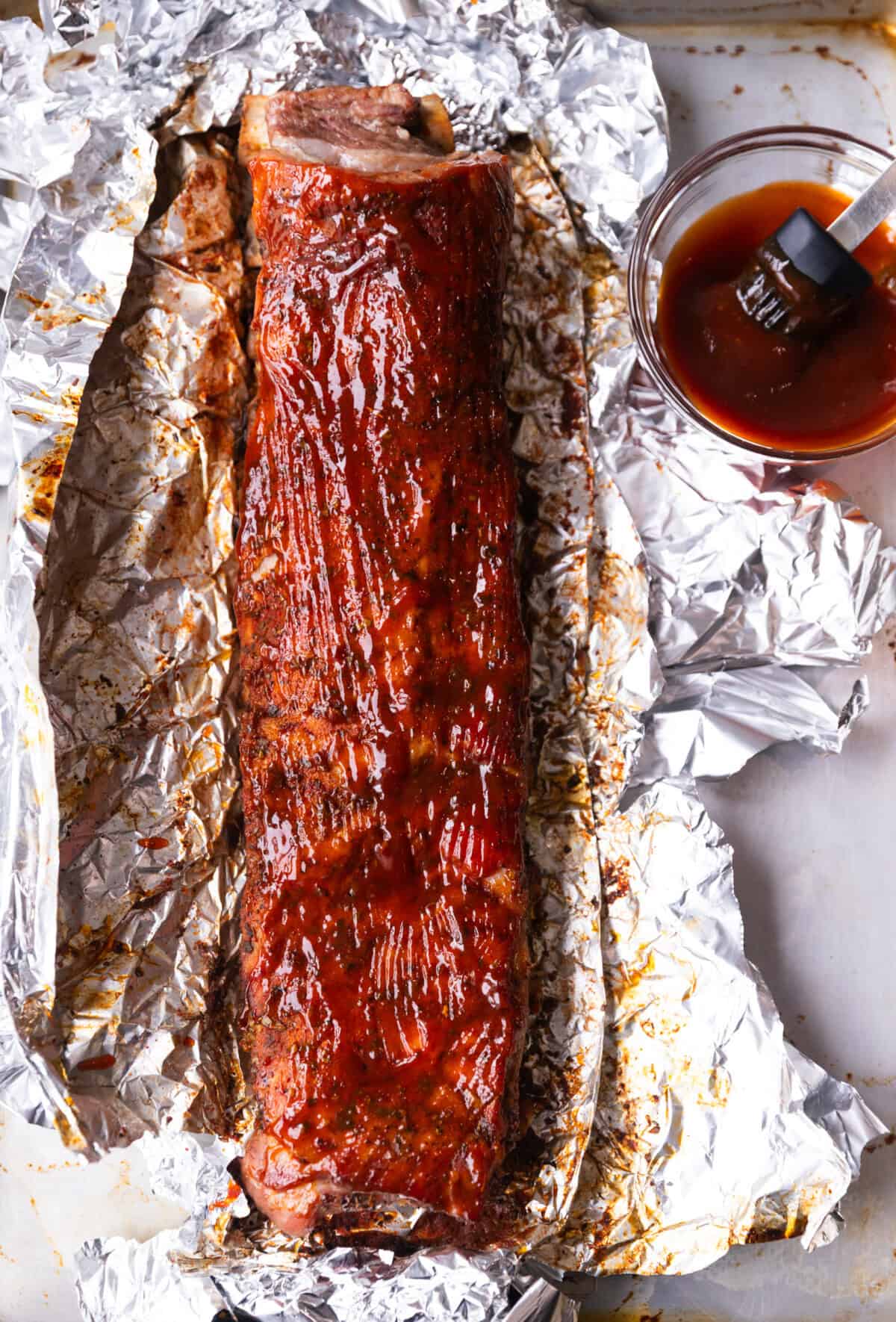 Oven baked St. Louis style ribs brushed with barbecue sauce on foil, ready to go back into the oven.
