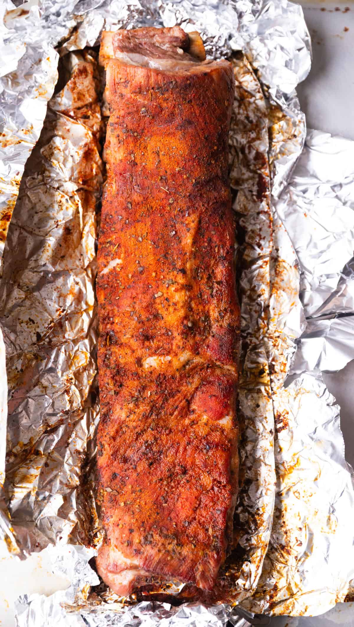 Partially cooked St. Louis ribs in foil, showing golden brown edges after baking.