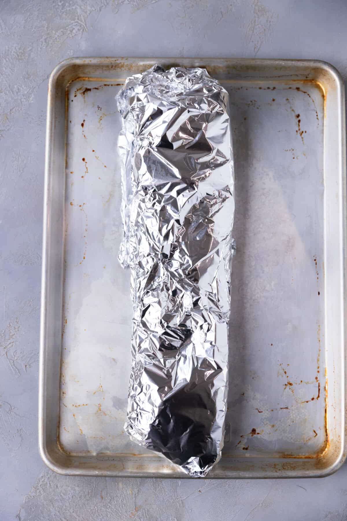 Rack of St. Louis style ribs tightly wrapped in foil on a baking sheet, ready for the oven