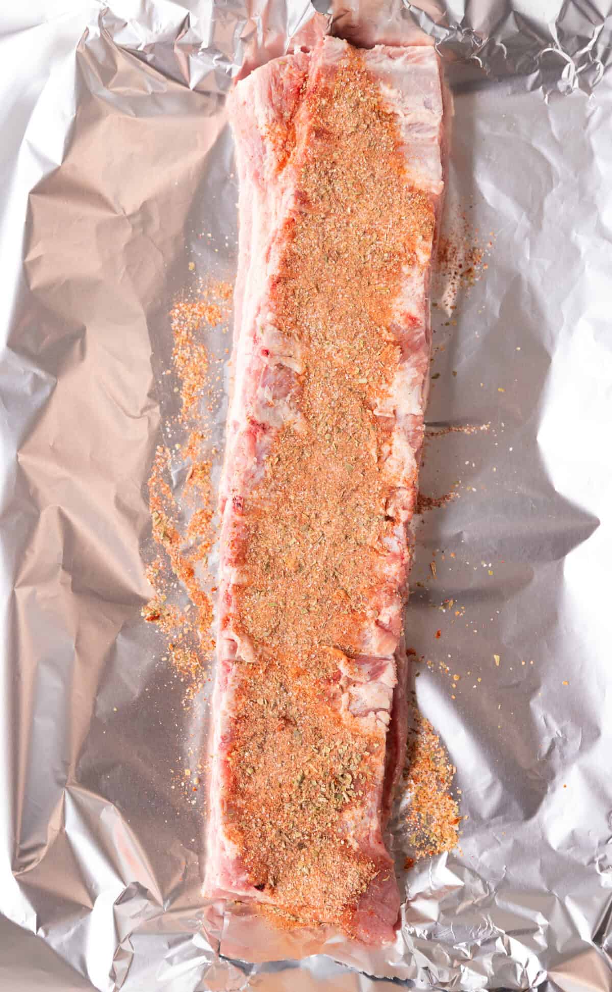 Raw St. Louis ribs coated with dry rub seasoning on both sides on top of aluminum foil, ready for the oven.