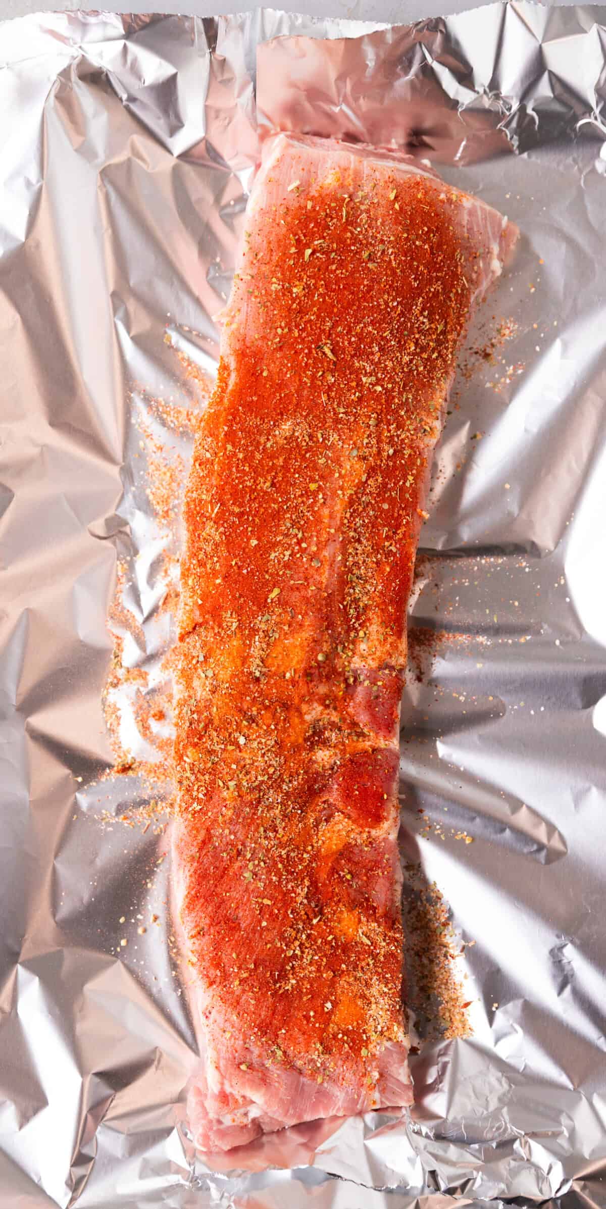 Raw St. Louis ribs coated with dry rub seasoning on top of aluminum foil, ready for the oven.