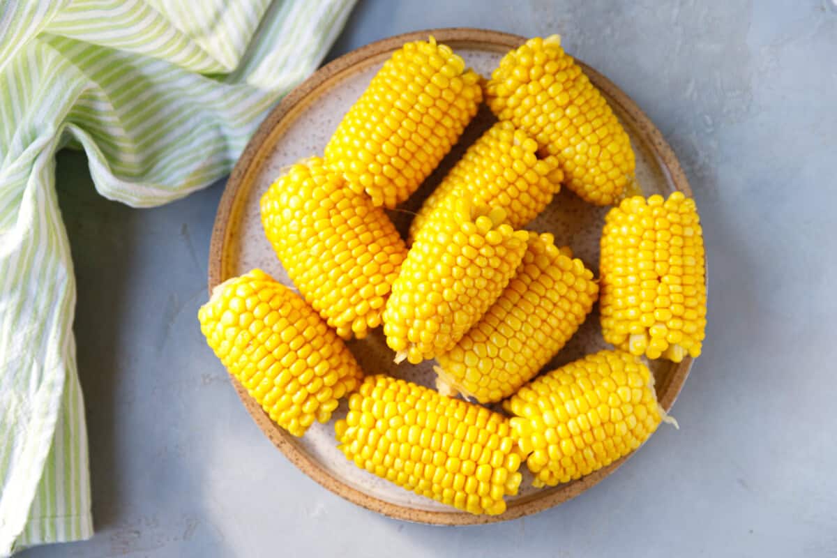Plate of freshly boiled corn on the cob pieces, bright yellow and glistening, ready to serve.