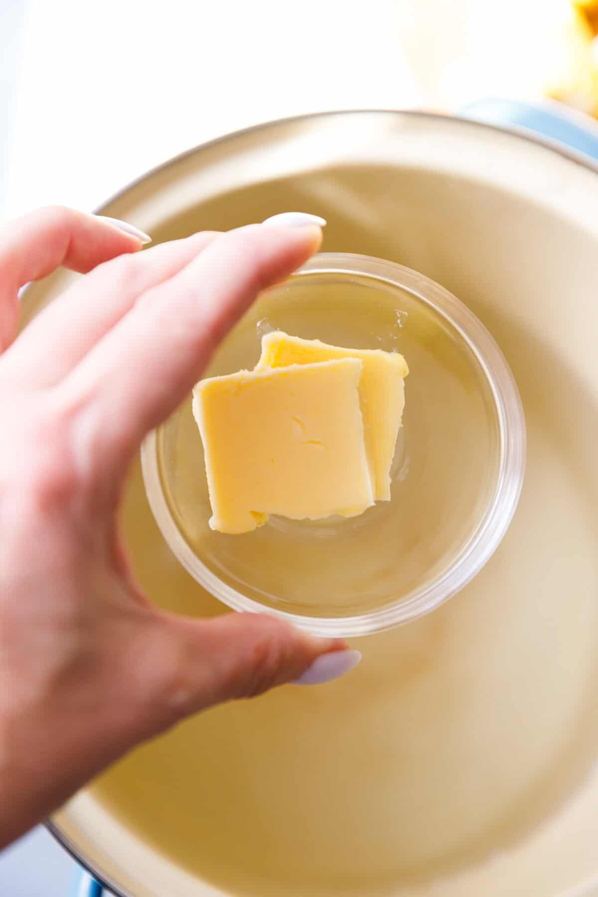 A hand holding a bowl with butter over a pot of water for boiling corn