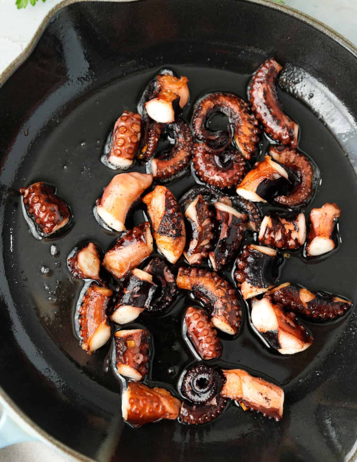 Octopus pieces searing in hot skillet with olive oil.