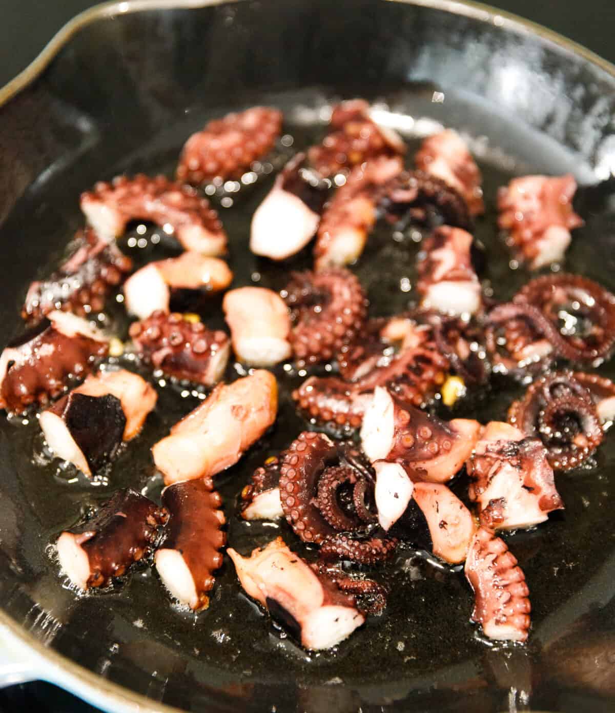 Octopus pieces searing in hot skillet with olive oil.