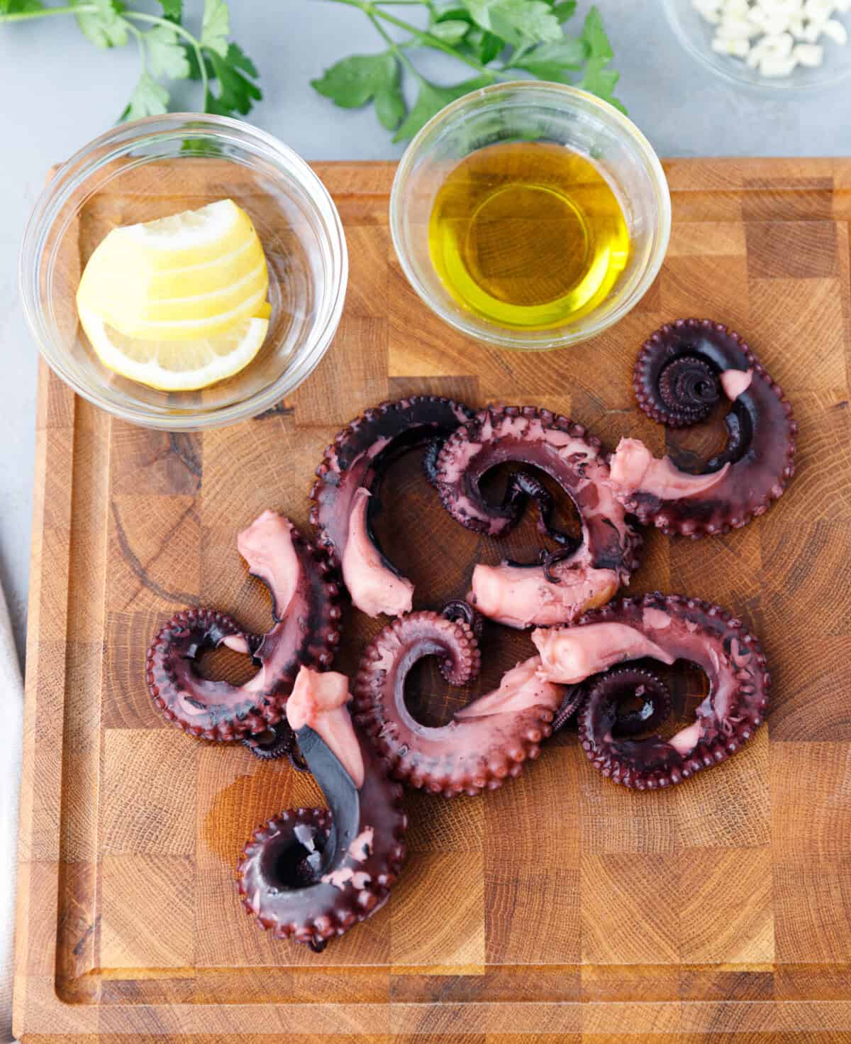 Cooked octopus tentacles drained on cutting board with lemon and olive oil.