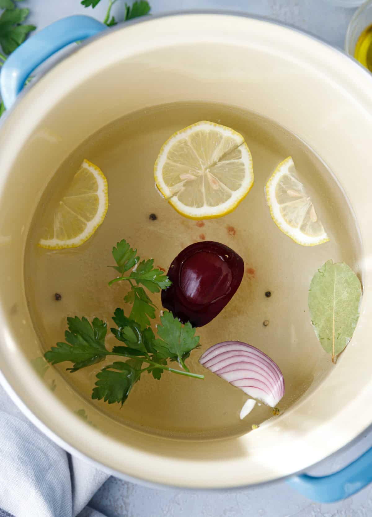 Pot filled with octopus, lemon slices, fresh parsley, bay leaf, and beet simmering in water to tenderize.