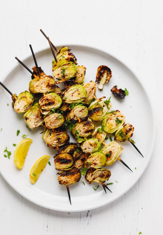 Grilled brussel sprouts on a wooden skewer on a plate with lemon wedger