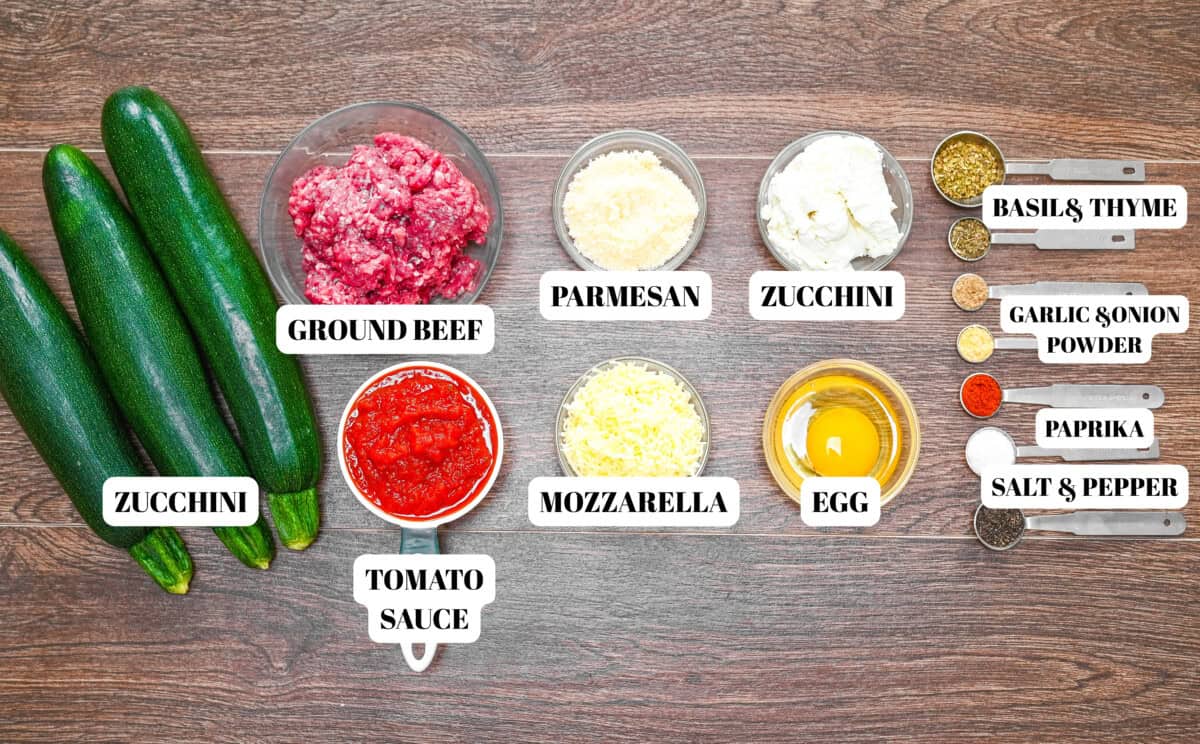 Flat lay of labeled ingredients for zucchini lasagna roll ups, including zucchini, ground beef, tomato sauce, mozzarella, parmesan, egg, ricotta, and dried spices.