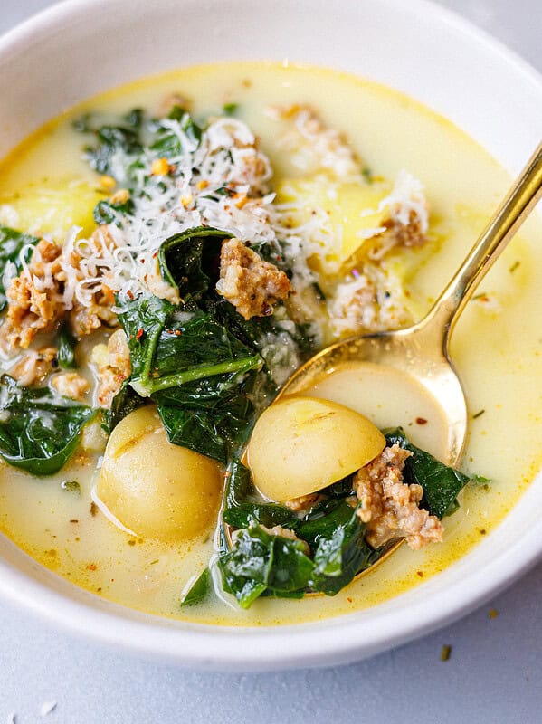 Close-up of sausage kale soup with a gold spoon lifting a baby potato and kale