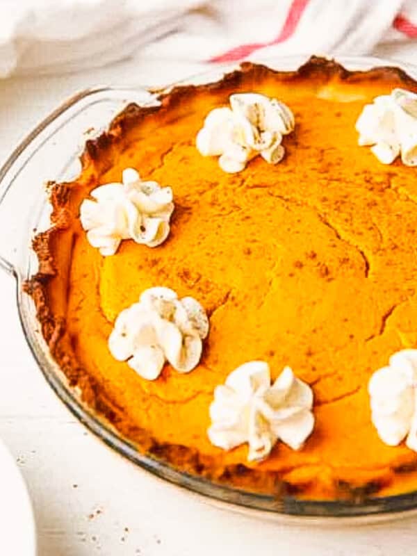 A whole keto pumpkin pie in a glass pie dish, decorated with dollops of whipped cream around the edge.