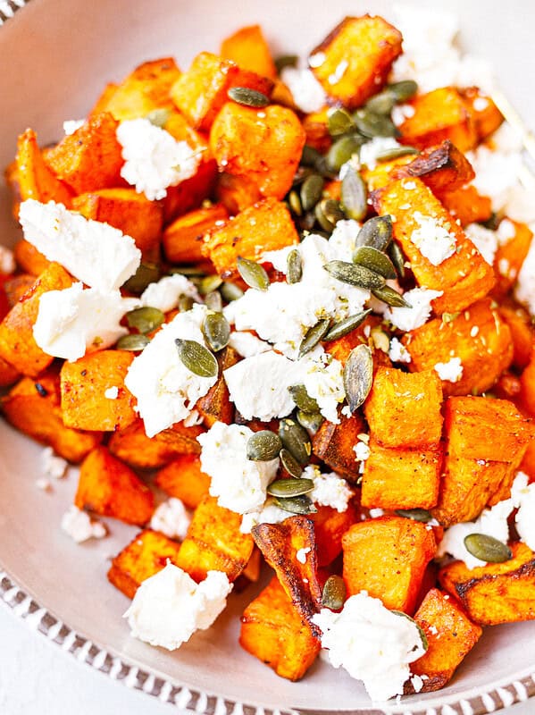 Close-up of roasted sweet potato cubes topped with crumbled feta, pumpkin seeds and dried oregano.