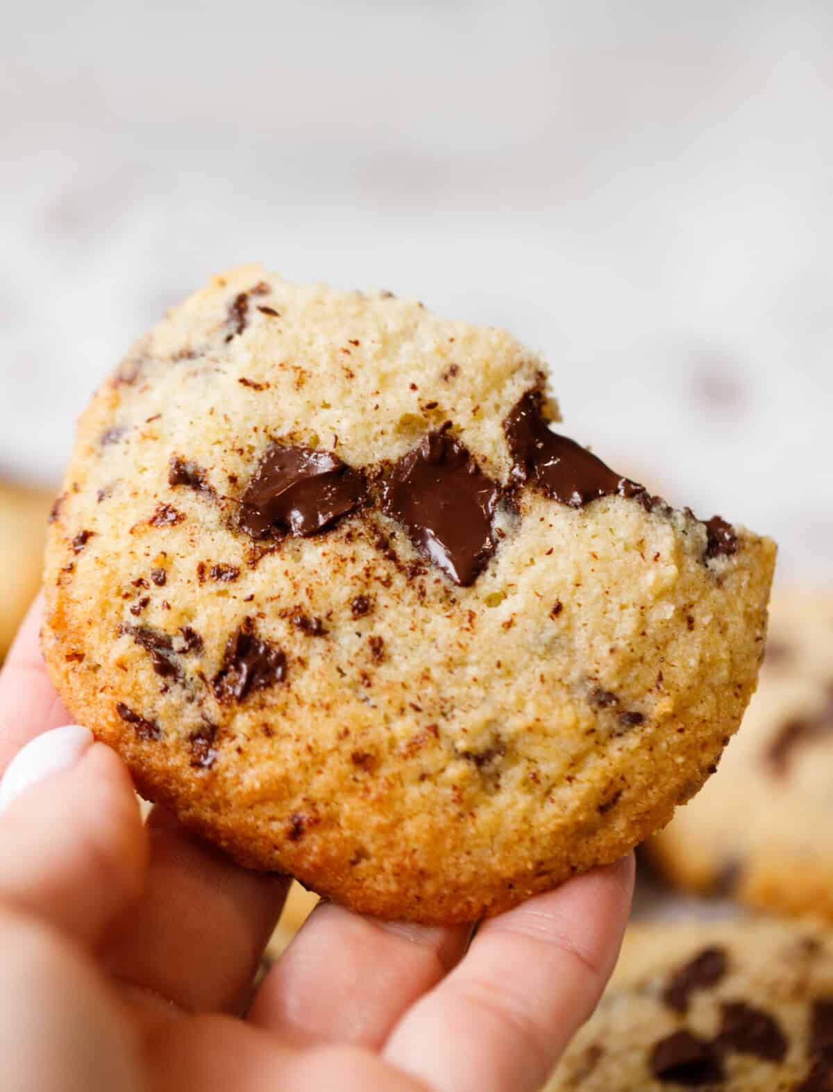 Low-carb chocolate chip cookie held in hand showing soft crumb and melted chocolate inside