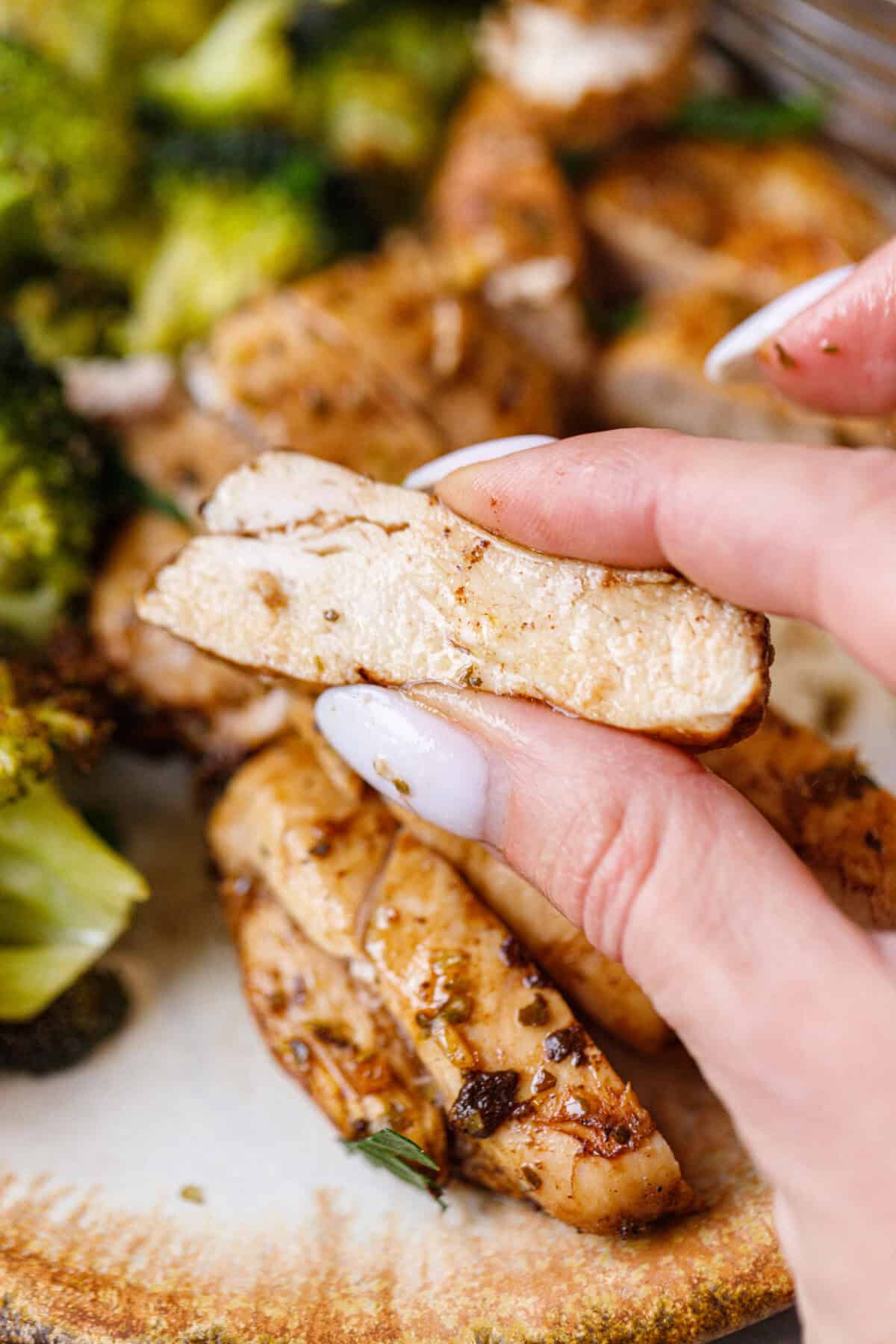 Hand holding a piece of baked balsamic chicken breast to show moist, perfectly cooked texture.
