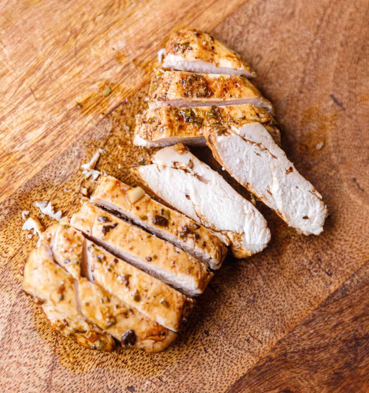 Sliced balsamic chicken breast on a wooden cutting board.