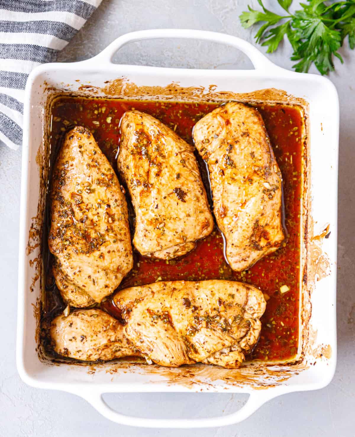 A white square baking dish with juicy baked balsamic chicken breasts inside.