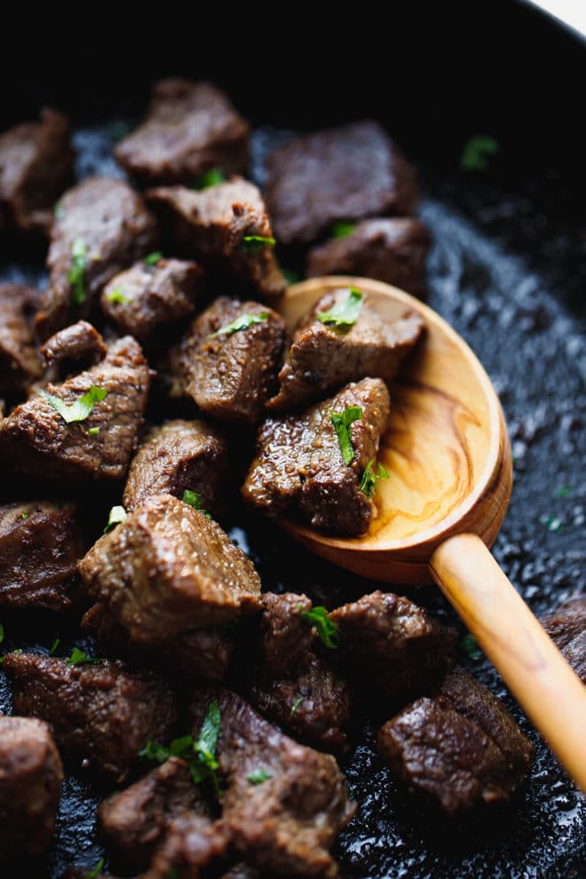Keto steak bites in a skillet with wooden spoon