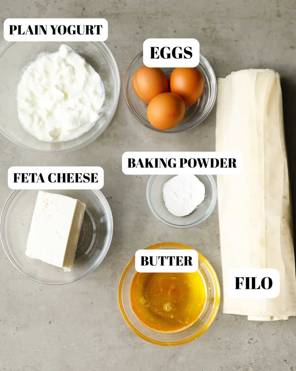 Bulgarian banitsa ingredients including phyllo dough, feta cheese, eggs, yogurt, baking powder and melted butter
