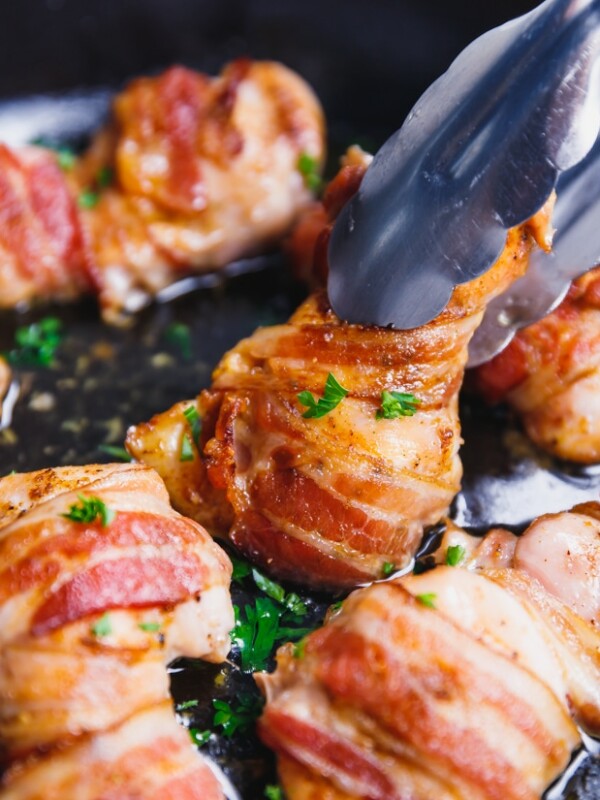 Thongs holding bacon wrapped chicken thighs