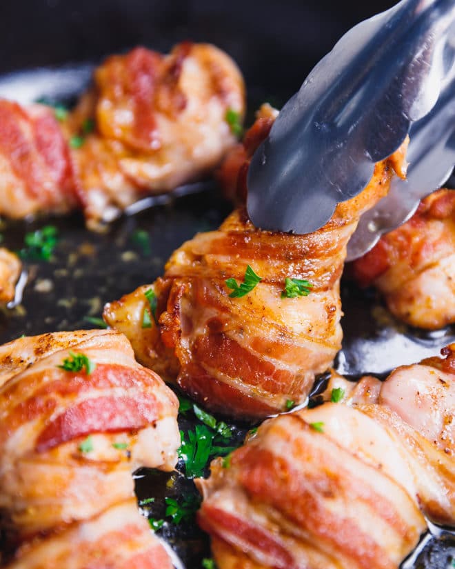 Thongs holding bacon wrapped chicken thighs