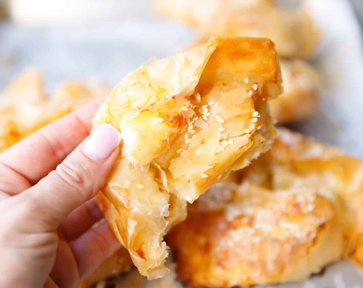 Hand holding a piece of flaky Bulgarian banitsa showing layers of phyllo dough and feta filling