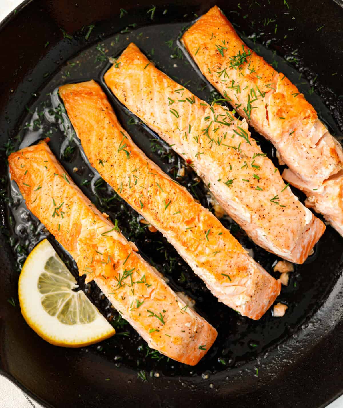 Pan seared salmon fillets with fresh dill and lemon in cast iron skillet