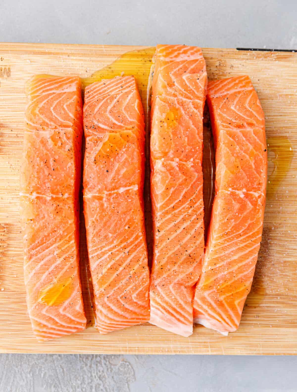 Raw salmon fillets seasoned with olive oil salt and pepper on wooden cutting board
