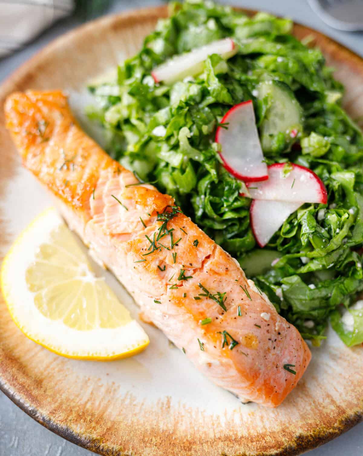 Pan seared salmon served with green salad and lemon on plate