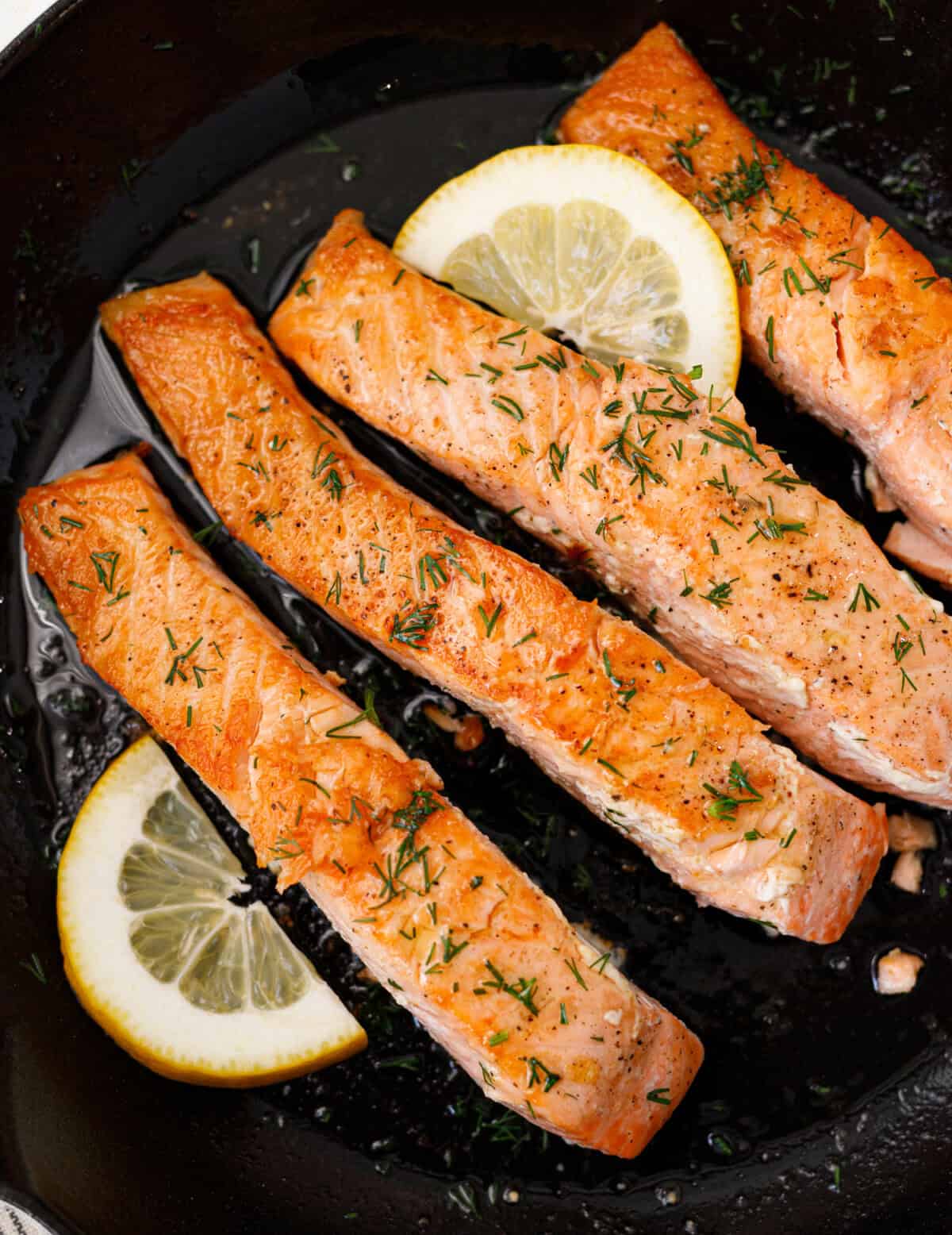 Golden pan seared salmon fillets in skillet with dill and lemon slice