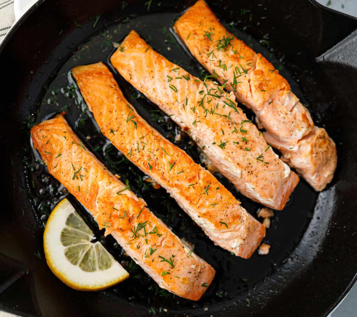 Pan seared salmon fillets with fresh dill and lemon in cast iron skillet