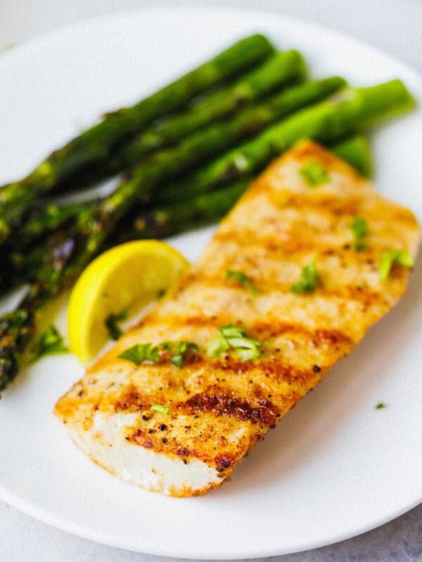Close-up of grilled mahi mahi showing golden grill marks and smoky spice crust, topped with fresh herbs