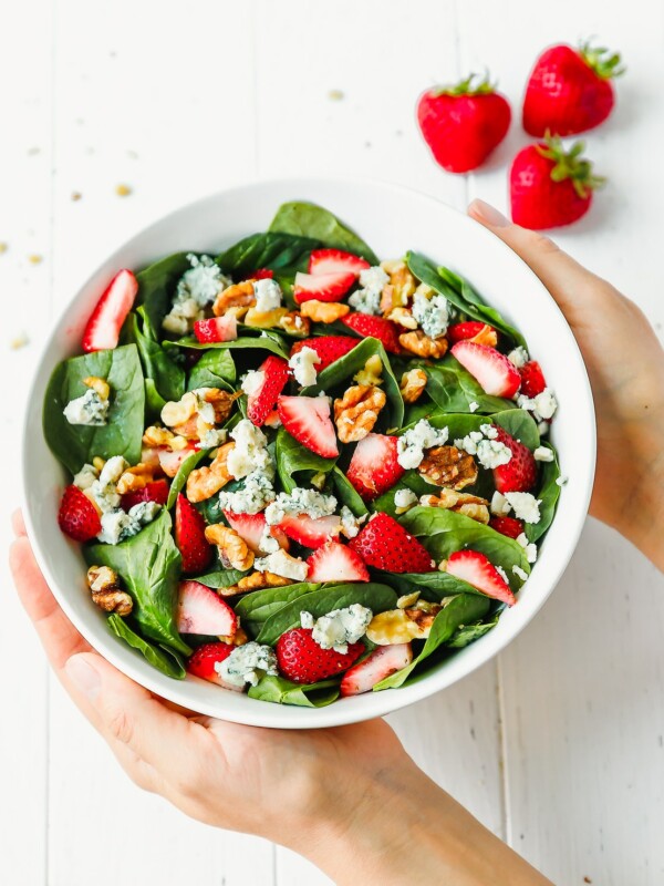 Hands holding a bowl of strawberry spinach salad