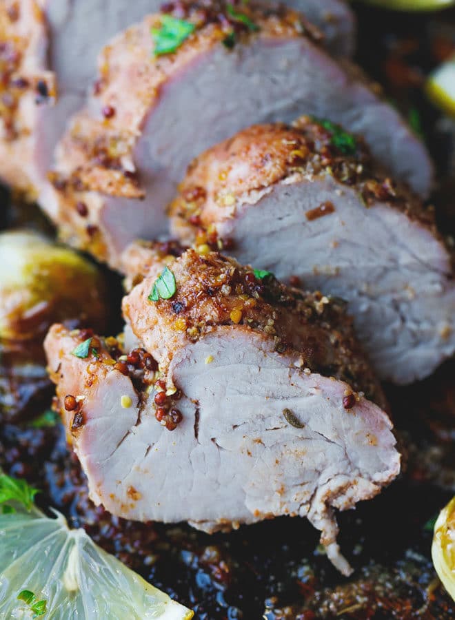 Sliced roasted pork tenderloin on a sheet pan with Brussel sprouts